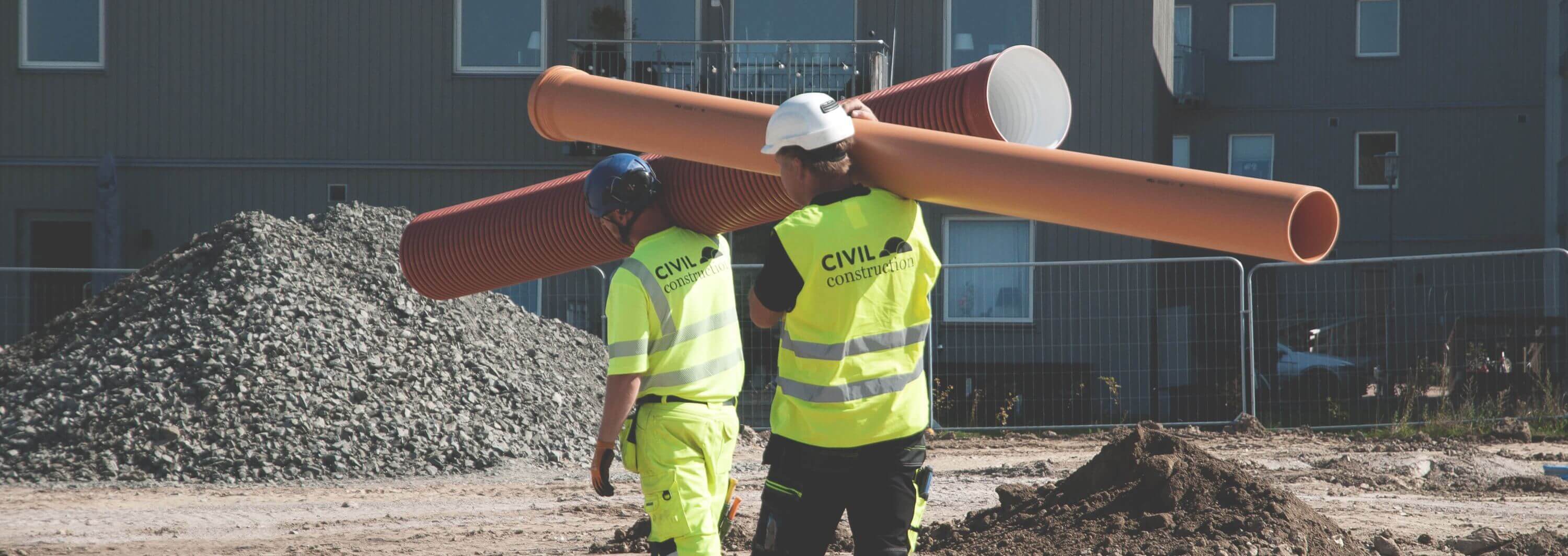 två personer bär stora rör till VA-arbete